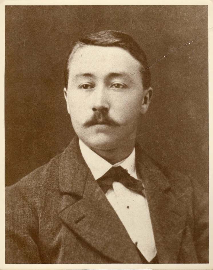 Sepia studio portrait of a mustached man, with surface marks and a diagonal scratch.