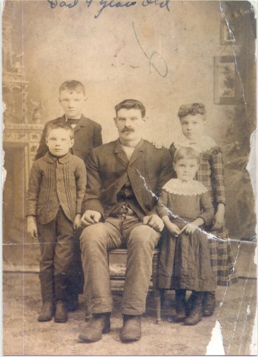 Sepia group portrait with a diagonal tear across the right side, handwritten marks and a missing area at the lower edge.